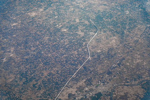 Aerial view of a vast agricultural landscape featuring a long straight canal cutting through dense grids of farm fields and small rural settlements in India. Aerial view of a vast agricultural landscape featuring a long straight canal cutting through dense grids of farm fields and small rural settlements in India.