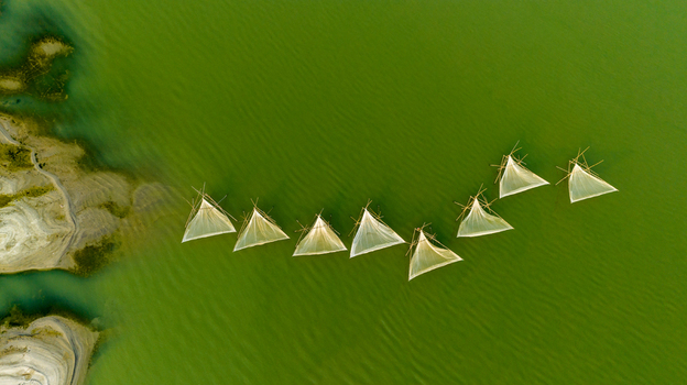 Aerial view of traditional triangular fishing nets arranged in a line on the calm green water of a river in Pabna Rajshahi Division Bangladesh.