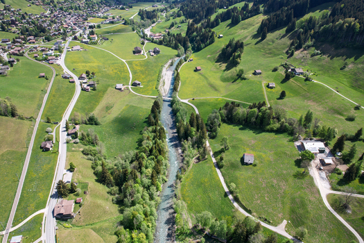 Aerial view of the Sarine river flowing through lush green meadows and scattered chalets in the valley Rougemont Vaud Switzerland. Aerial view of the Sarine river flowing through lush green meadows and scattered chalets in the valley Rougemont Vaud Switzerland.