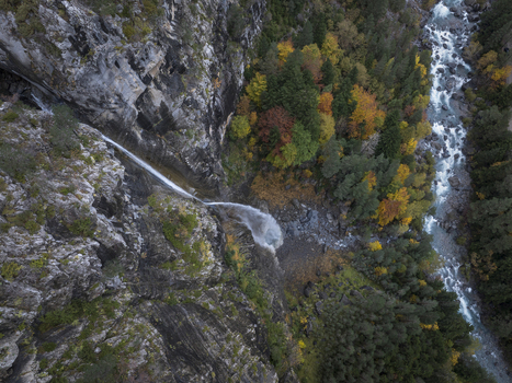Aerial view of a waterfall cascading down a rocky cliff face into a forest with a river flowing nearby in the Pyrenees Spain. Aerial view of a waterfall cascading down a rocky cliff face into a forest with a river flowing nearby in the Pyrenees Spain.