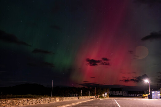 View of the Aurora Borealis illuminating the night sky with vibrant green and red lights above a coastal road and stone wall in Portnoo County Donegal Ireland. View of the Aurora Borealis illuminating the night sky with vibrant green and red lights above a coastal road and stone wall in Portnoo County Donegal Ireland.