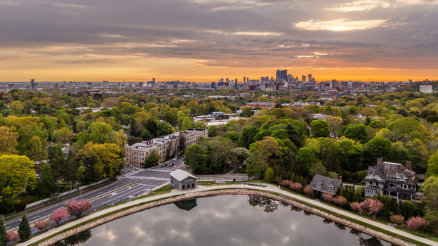 Aerial view of Brookline Reservoir surrounded by lush spring cherry trees and residential houses with the Boston skyline in the distance at sunrise. Brookline Massachusetts United States.