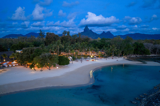 Aerial view of a luxury beach resort with illuminated palm trees and white sand under a twilight sky with the Moka Range mountains in the background Moka District Mauritius. Aerial view of a luxury beach resort with illuminated palm trees and white sand under a twilight sky with the Moka Range mountains in the background Moka District Mauritius.