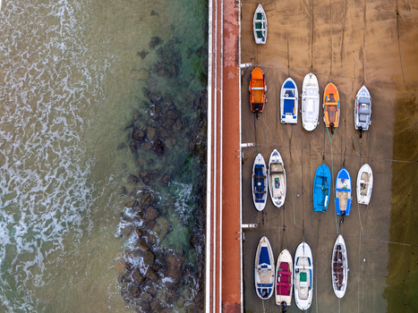 Aerial view of Puerto de Zarautz with colorful fishing boats moored along a stone pier with clear water and rocky shoreline in Zarautz Basque Country Spain.