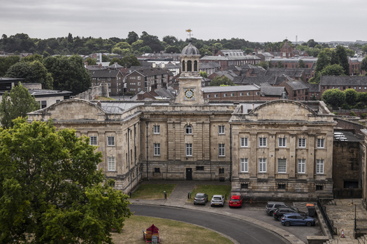 Aerial view of the historic York Castle Museum with its prominent clock tower surrounded by urban rooftops and parked cars in York England United Kingdom.