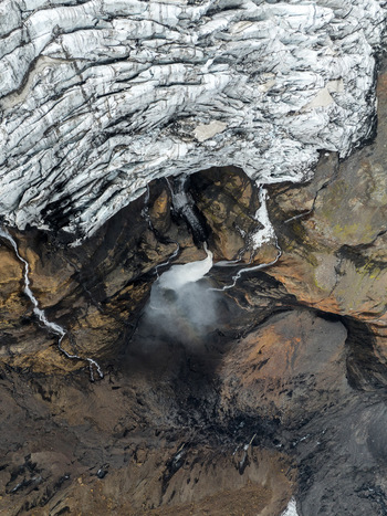 Aerial view of a glacier meltwater waterfall cascading down a dark volcanic rock face with ice formations in Vik Myrdalshreppur Iceland.