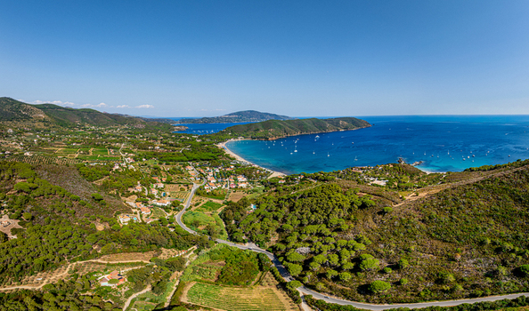 Aerial view of Lacona Beach featuring a sandy coastline turquoise waters with anchored boats surrounded by lush green hills and Mediterranean vegetation in Lacona Tuscany Italy.
