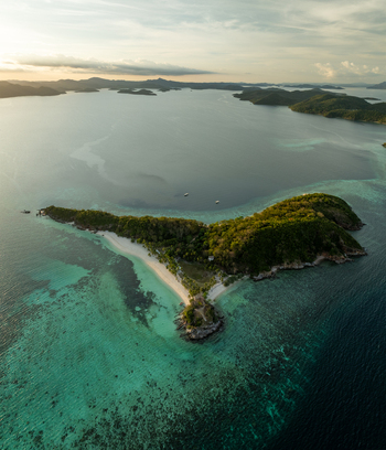 Aerial view of Malcapuya Island featuring lush tropical vegetation white sand beaches and turquoise coral reefs surrounded by deep blue sea in Coron Mimaropa Philippines. Aerial view of Malcapuya Island featuring lush tropical vegetation white sand beaches and turquoise coral reefs surrounded by deep blue sea in Coron Mimaropa Philippines.
