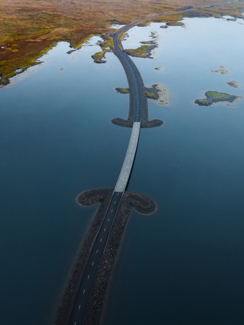 Aerial view of a striking road cuts through the tranquil waters a ribbon of grey against the deep blue connecting patches of land under the expansive sky Westfjords Iceland. Aerial view of a striking road cuts through the tranquil waters a ribbon of grey against the deep blue connecting patches of land under the expansive sky Westfjords Iceland.