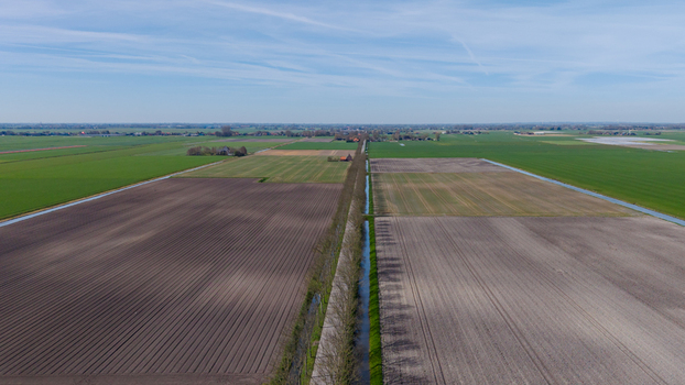 Aerial view of rich dark soil meeting vibrant green fields across the flat landscape divided by a slim canal Lambertschaag North Holland Netherlands. Aerial view of rich dark soil meeting vibrant green fields across the flat landscape divided by a slim canal Lambertschaag North Holland Netherlands.