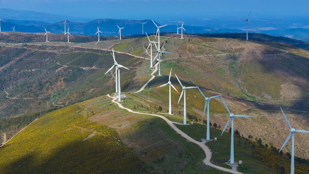 Aerial view of wind turbines situated on rolling hills with green vegetation and dirt access paths under a clear blue sky in Lisbon Lisbon Portugal. Aerial view of wind turbines situated on rolling hills with green vegetation and dirt access paths under a clear blue sky in Lisbon Lisbon Portugal.