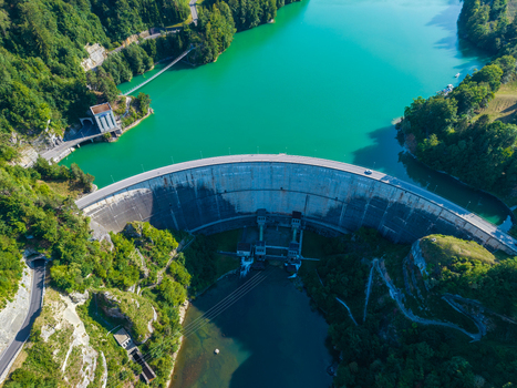 Aerial view of Barrage de Rossens a concrete dam holding back turquoise reservoir waters surrounded by dense forests and winding roads in Pont la Ville Fribourg Switzerland.
