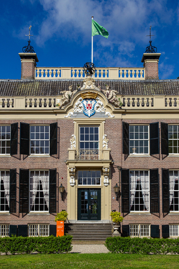 View of the ornate facade of Castle Groeneveld with its historic brickwork black shutters and decorative stone carvings under a blue sky in Baarn Utrecht Netherlands.