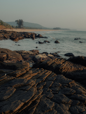 View of dark textured rocks leading to a sandy beach where the sea meets the shore under a hazy sky a tranquil scene Chiplun Maharashtra India. View of dark textured rocks leading to a sandy beach where the sea meets the shore under a hazy sky a tranquil scene Chiplun Maharashtra India.
