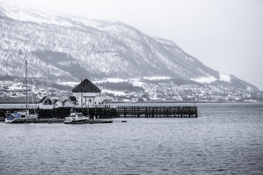 View of the waterfront with wooden buildings and boats against snow covered mountains under an overcast sky Tromso Troms Norway. View of the waterfront with wooden buildings and boats against snow covered mountains under an overcast sky Tromso Troms Norway.