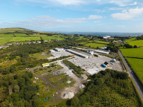 Aerial view of an industrial site with stone storage warehouse buildings and trucks surrounded by green rolling hills and rural farmland in Lisburn Northern Ireland United Kingdom. Aerial view of an industrial site with stone storage warehouse buildings and trucks surrounded by green rolling hills and rural farmland in Lisburn Northern Ireland United Kingdom.