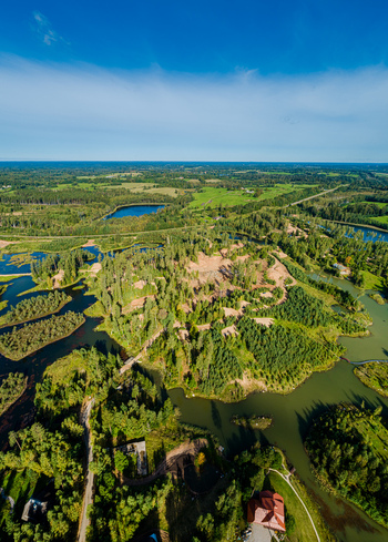 Aerial view of lush green forests winding ponds and sandy terrain patches under a clear blue sky in Latvia. Aerial view of lush green forests winding ponds and sandy terrain patches under a clear blue sky in Latvia.