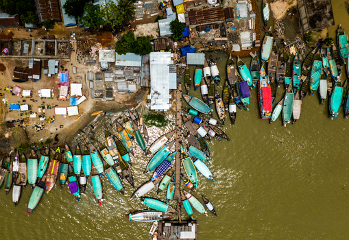 Aerial view of Baish Mowza Sarak Bazar featuring numerous colorful wooden boats docked along the riverbank near bustling market stalls in Nabinagar Chittagong Division Bangladesh. Aerial view of Baish Mowza Sarak Bazar featuring numerous colorful wooden boats docked along the riverbank near bustling market stalls in Nabinagar Chittagong Division Bangladesh.