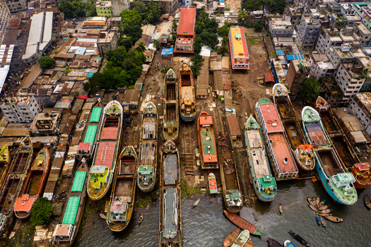 Aerial view of a busy shipyard with numerous cargo ships and boats docked for maintenance along the riverbank surrounded by dense urban buildings in Dhaka Dhaka Division Bangladesh.