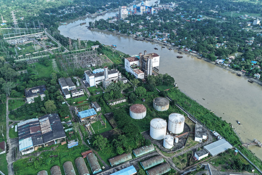 Aerial view of the Karnaphuli River flowing past an industrial complex with storage tanks and power infrastructure in Chattogram Chittagong Division Bangladesh.