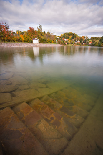 View of Velka Richnava lake with submerged stone steps autumn foliage on the hills and a small building on the bank in Stiavnicke Bane Banska Bystrica Region Slovakia.