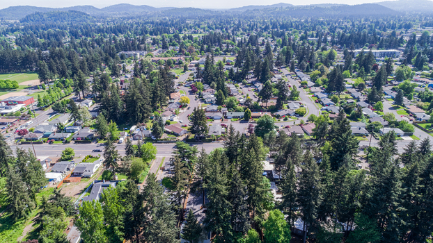Aerial view of Northeast Glisan Street running through a lush residential neighborhood with tall evergreen trees and distant hills in Portland Oregon United States. Aerial view of Northeast Glisan Street running through a lush residential neighborhood with tall evergreen trees and distant hills in Portland Oregon United States.