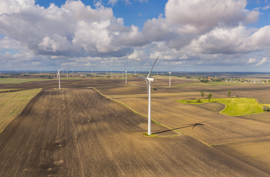 Aerial view of wind turbines in a vast agricultural field under a cloudy sky in Pomeranian Voivodeship Poland.