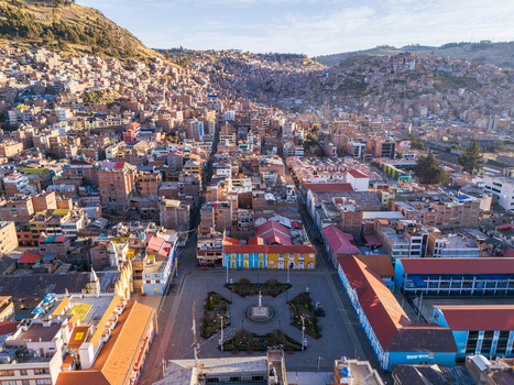 Aerial view of the central square and surrounding urban landscape of Puno with dense residential buildings climbing the hillsides under a clear blue sky in Puno Puno Peru.