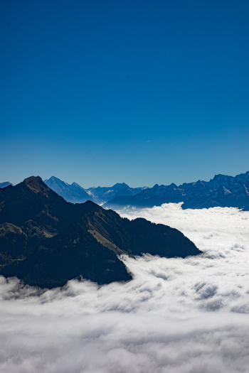 Aerial view of the Swiss Alps with rugged mountain peaks rising above a dense sea of clouds under a clear blue sky in Airolo Ticino Switzerland. Aerial view of the Swiss Alps with rugged mountain peaks rising above a dense sea of clouds under a clear blue sky in Airolo Ticino Switzerland.