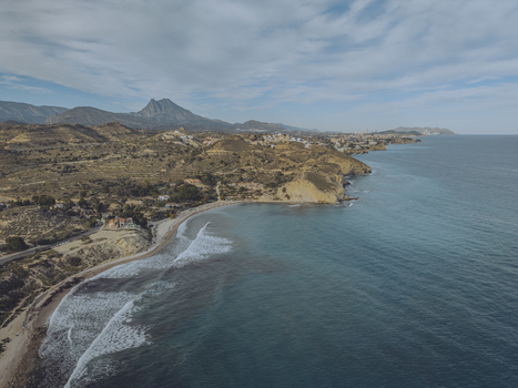 Aerial view of Torre del Xarco on a rugged cliff overlooking the Mediterranean Sea with sandy beaches rolling hills and distant mountains under a cloudy sky La Vila Joiosa Comunidad Valenciana Spain.