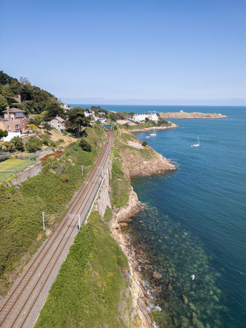 Aerial view of the Dalkey coastline featuring railway tracks running along the cliffs lush greenery and the blue sea in Dublin County Dublin Ireland. Aerial view of the Dalkey coastline featuring railway tracks running along the cliffs lush greenery and the blue sea in Dublin County Dublin Ireland.
