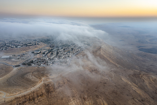 Aerial view of the Mitzpe Ramon crater rim with low hanging clouds rolling over the town of Mitzpe Ramon in the Negev desert Mitzpe Ramon South District Israel. Aerial view of the Mitzpe Ramon crater rim with low hanging clouds rolling over the town of Mitzpe Ramon in the Negev desert Mitzpe Ramon South District Israel.