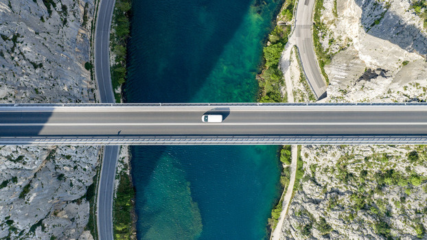 Aerial view of a white van driving across a modern bridge over the turquoise Cetina River canyon between steep rocky cliffs in Omis Split Dalmatia County Croatia. Aerial view of a white van driving across a modern bridge over the turquoise Cetina River canyon between steep rocky cliffs in Omis Split Dalmatia County Croatia.