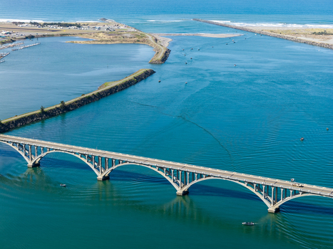 Aerial view of the Isaac Lee Patterson Bridge spanning the Rogue River with boats in the water and coastal landscape in Gold Beach Oregon United States. Aerial view of the Isaac Lee Patterson Bridge spanning the Rogue River with boats in the water and coastal landscape in Gold Beach Oregon United States.