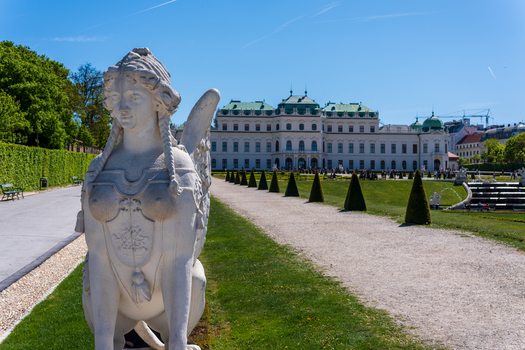 View of Belvedere Palace with a sphinx statue manicured gardens and a gravel path under a clear blue sky in Vienna Austria. View of Belvedere Palace with a sphinx statue manicured gardens and a gravel path under a clear blue sky in Vienna Austria.