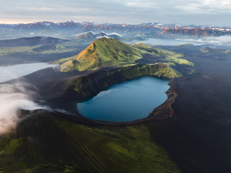 Aerial view of the serene blue lake nestled within the dark volcanic crater surrounded by green mossy hills Highlands Iceland.
