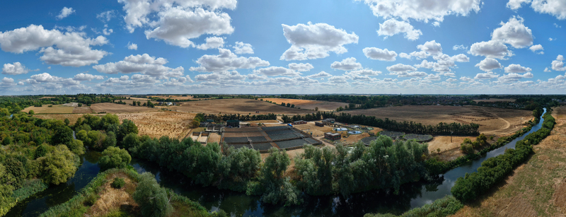 Aerial view of the wastewater treatment works along a river surrounded by trees and agricultural fields under a blue sky with clouds in St Neots England United Kingdom. Aerial view of the wastewater treatment works along a river surrounded by trees and agricultural fields under a blue sky with clouds in St Neots England United Kingdom.