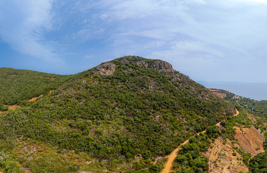 Aerial view of the historic iron mine area geology near Laghetto delle conche featuring rugged hills covered in Mediterranean scrub and a winding dirt path in Rio Marina Toscana Italy.