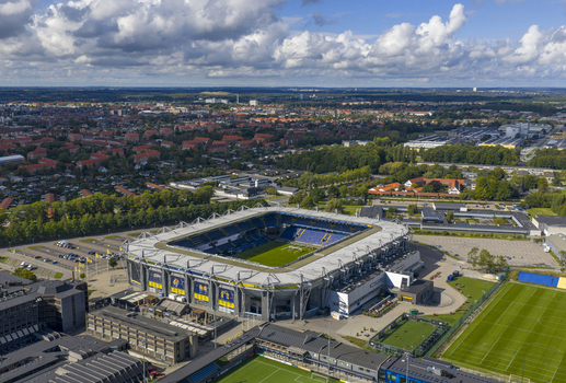Aerial view of Brondby Stadium with its distinctive blue and yellow seating and green pitch under a cloudy sky in Brondby Denmark.