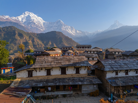 Aerial view of a traditional Himalayan village with stone roofed houses nestled against the backdrop of the snow capped Annapurna mountain range in Nepal.