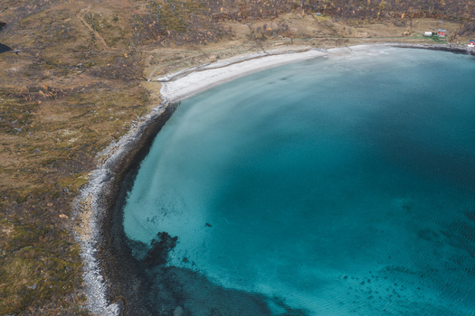 Aerial view of the turquoise waters of a beach surrounded by rocky coastline and autumn colored vegetation in Senja Troms Norway.