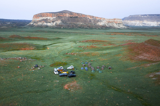 Aerial view of the Airakty mountains with a campsite featuring tents and off road vehicles set in the vast green steppe landscape of Shetpe Mangystau Region Kazakhstan.