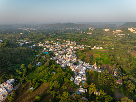 Aerial view of a small village nestled among lush green hills and fields in Udaipur Rajasthan India.