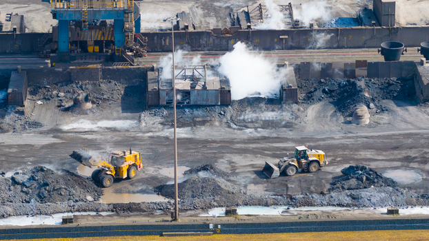 Aerial view of the Tata Steel industrial site with wheel loaders operating near piles of raw materials and rising steam in Velsen Noord Noord Holland Netherlands. Aerial view of the Tata Steel industrial site with wheel loaders operating near piles of raw materials and rising steam in Velsen Noord Noord Holland Netherlands.