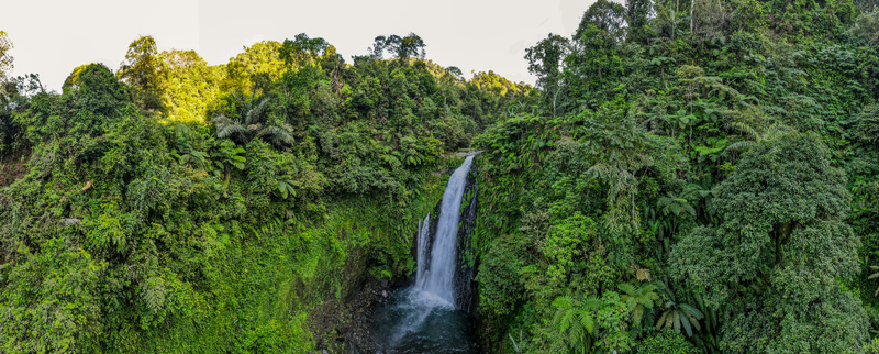 Aerial view of Gomblang Waterfall cascading into a pool surrounded by dense tropical jungle and lush green foliage in Kecamatan Kedungbanteng Jawa Tengah Indonesia. Aerial view of Gomblang Waterfall cascading into a pool surrounded by dense tropical jungle and lush green foliage in Kecamatan Kedungbanteng Jawa Tengah Indonesia.