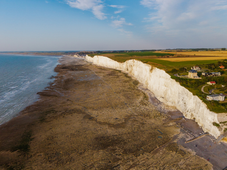 Aerial view of the white chalk cliffs and the beach of the Bois de Cise along the coastline with green fields and houses in Ault Hauts de France France.