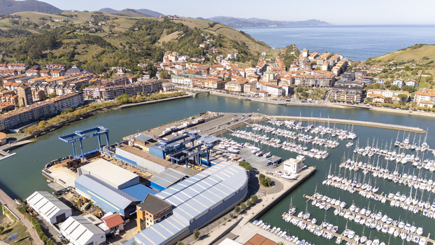 Aerial view of the marina and harbor in Zumaia featuring rows of docked sailboats shipyard facilities and the town nestled against green hills in Zumaia Basque Country Spain.