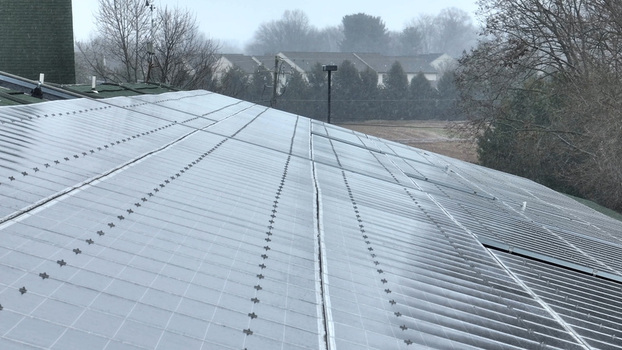 Aerial view of solar panels on a residential roof during a winter snowstorm with houses in the background in Neffsville Pennsylvania United States.