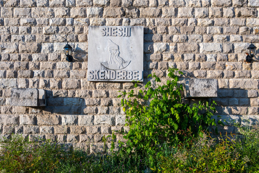 View of the Sheshi Skenderbej marble plaque with a relief of Skanderbeg on a textured stone wall with lanterns and green bushes in Kruje Durres County Albania.