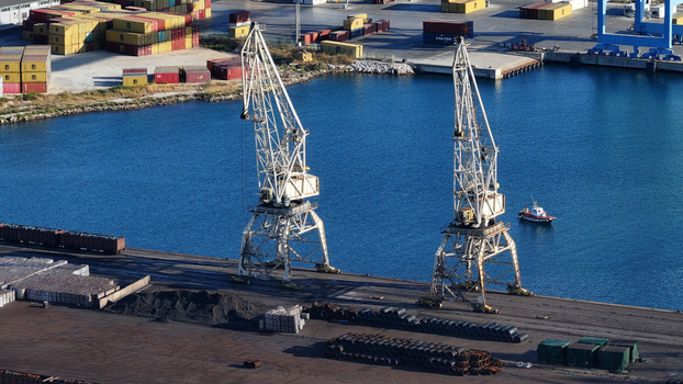 Aerial view of the Port of Ploce featuring two large harbor cranes stacks of shipping containers industrial cargo and a small boat navigating the harbor waters in Croatia.